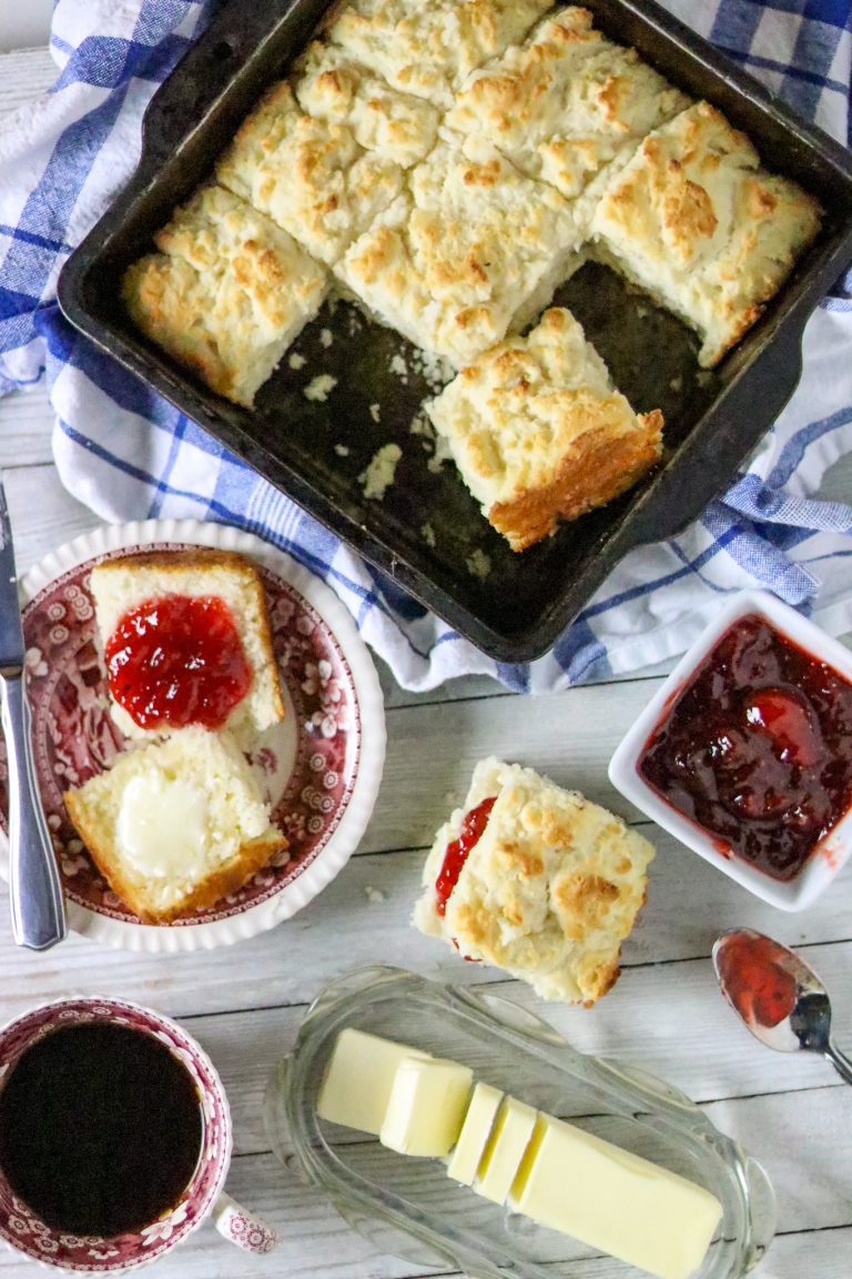 A pan of biscuits with a buttered biscuit with jam on a plate next to it.