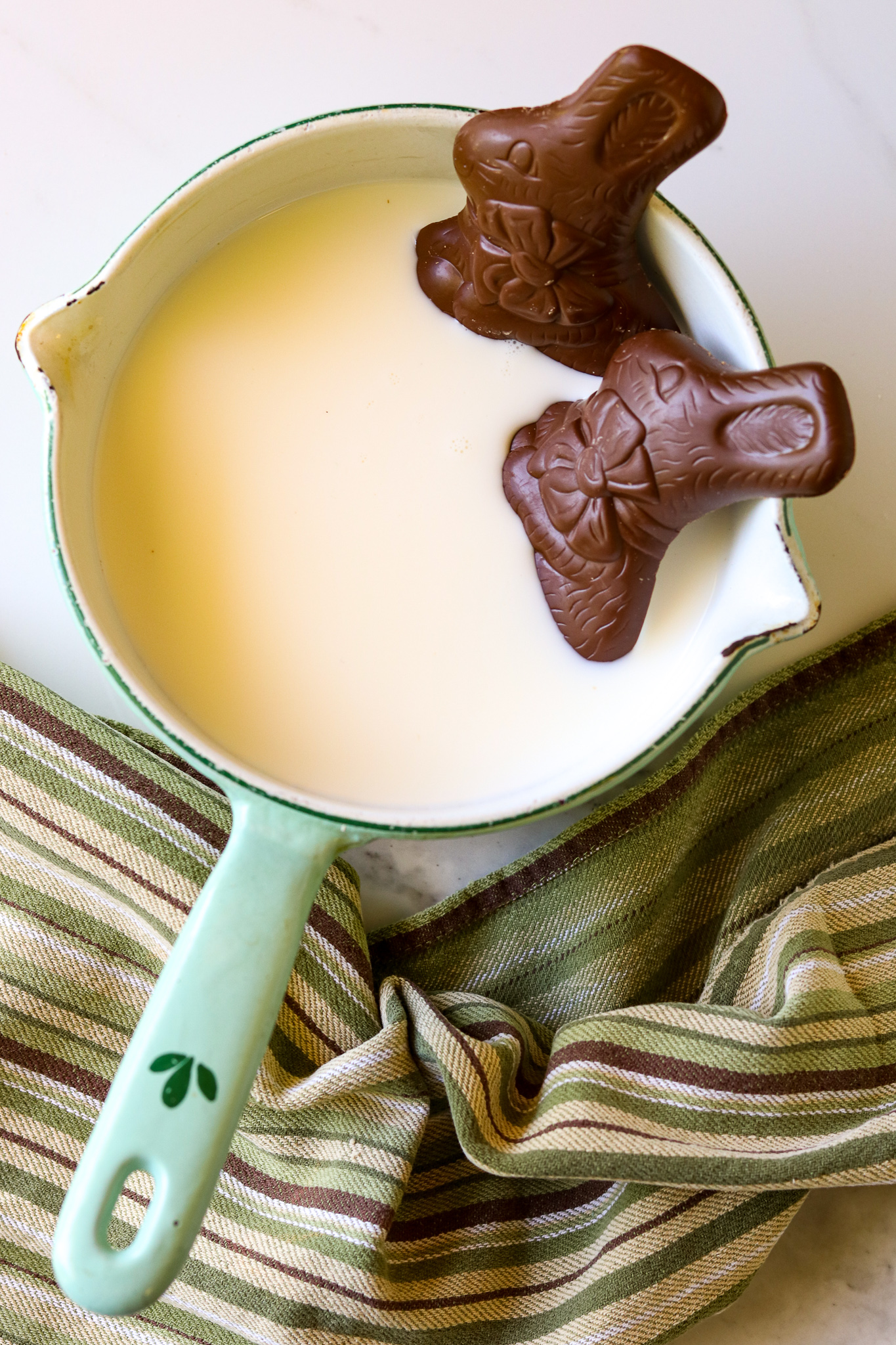 A sauce pan with milk and 2 chocolate Easter bunnies in it.
