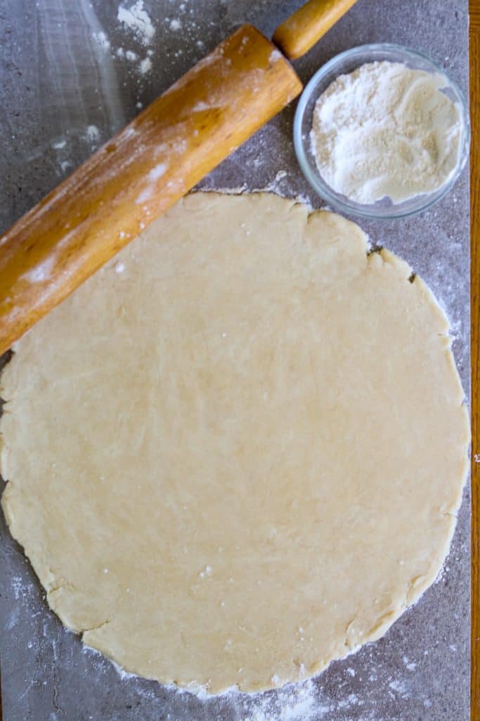 Rolled out circle of pie crust with rolling pin.