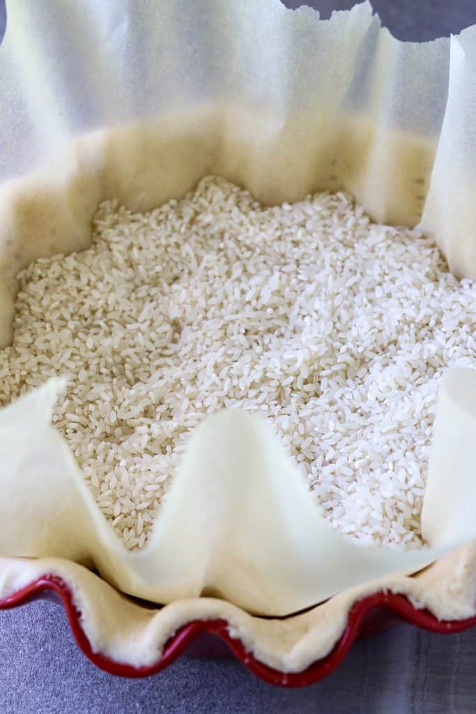 Unbaked pie shell for filled with rice on a parchment paper in How To Make A Pie Crust.