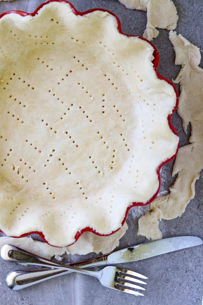 Unbaked pie crust in a red fluted pie plate pricked with a fork.