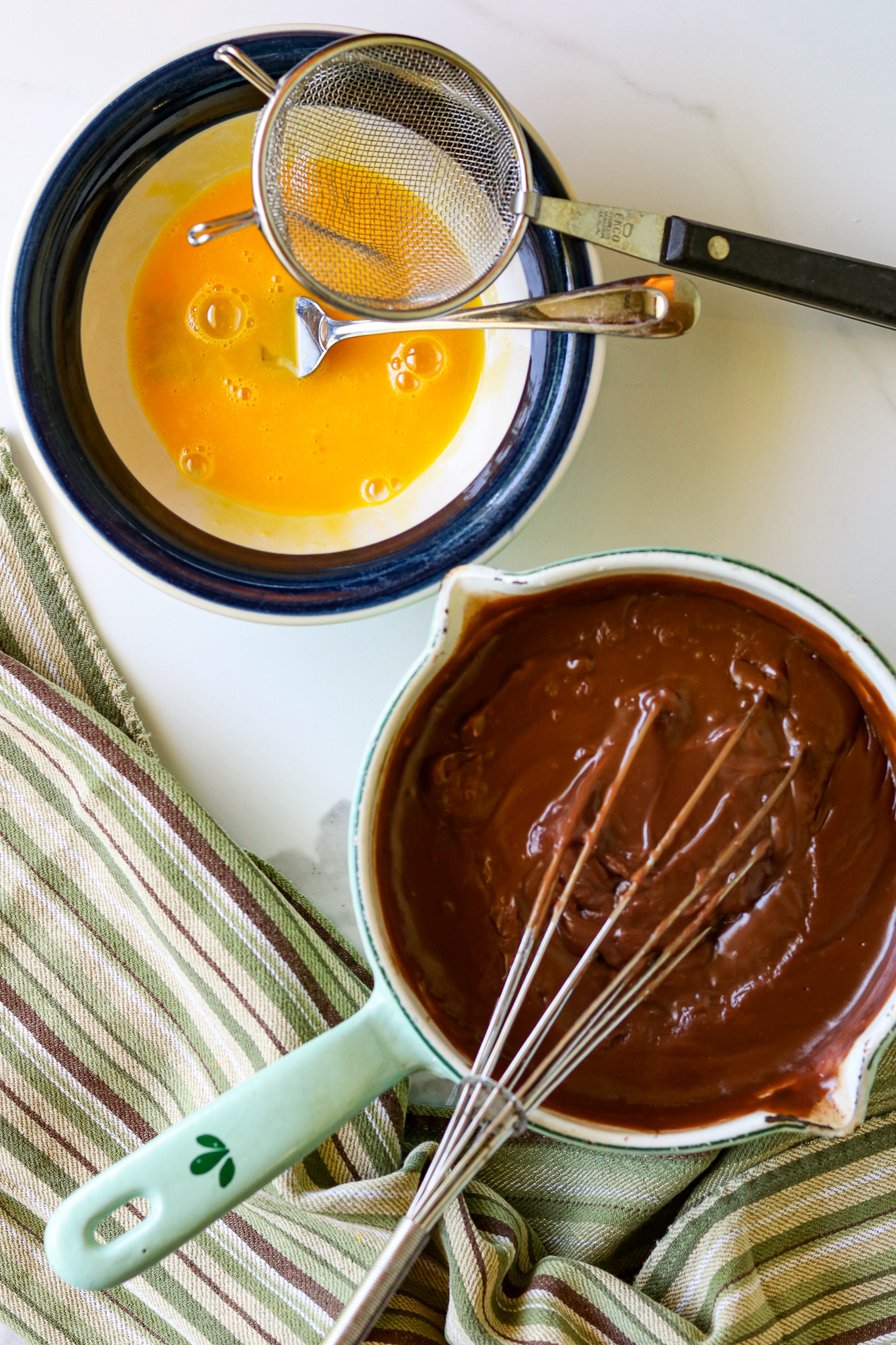 A bowl lwith egg yolks and a strainer next to a saucepan of Chocolate Bunny Pie filling in it.