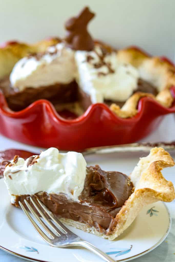 A chocolate pie with a chocolate bunny on top and a pice of pie cut out on a plate.