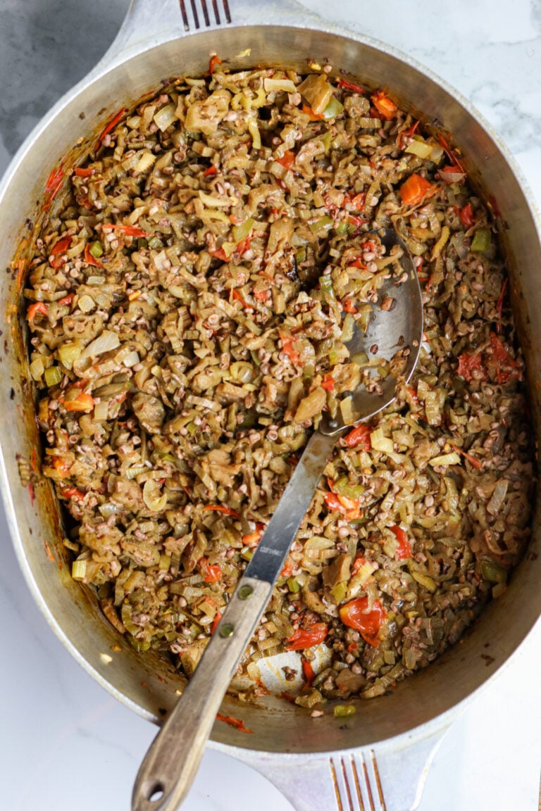 Cooked okra with tomatoes in a pot with a long-handled silver spoon.