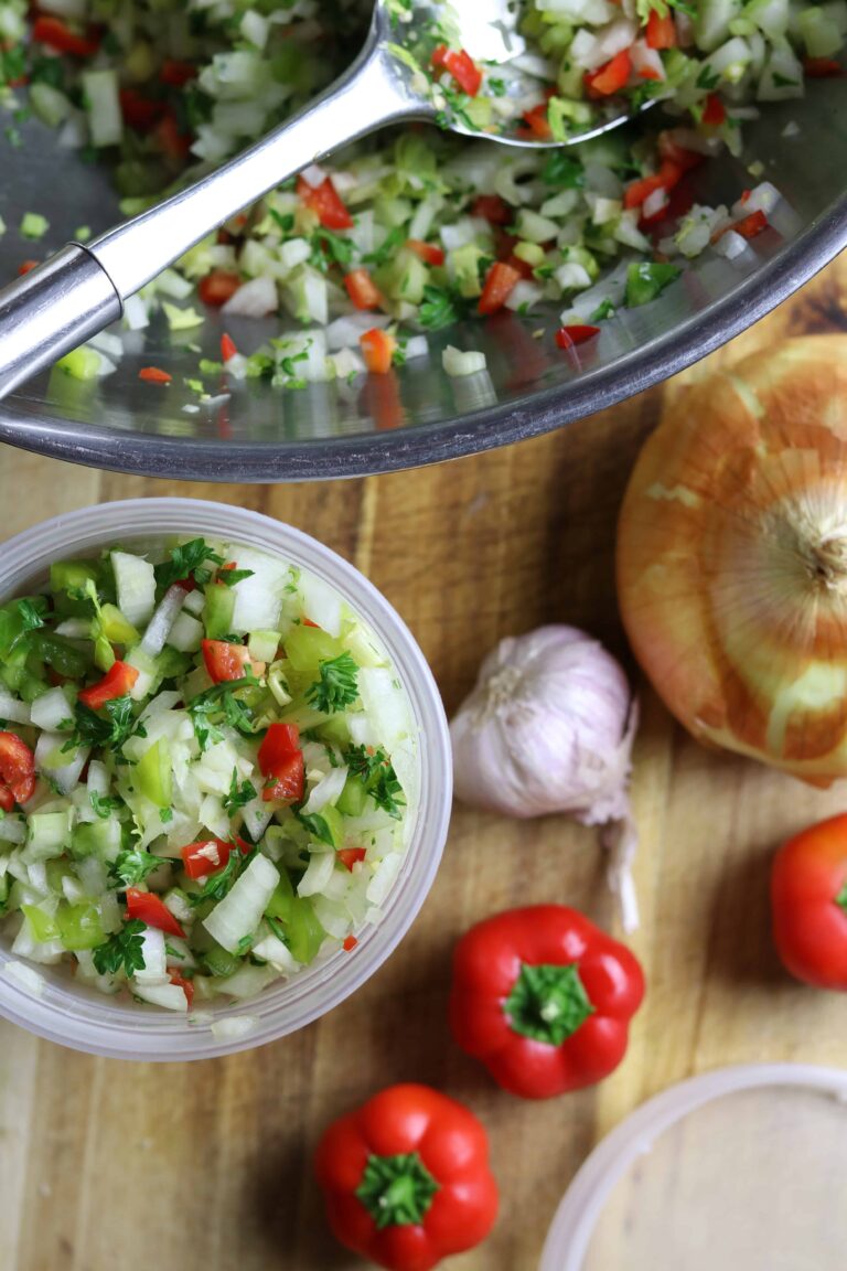 A bowl of chopped vegetables with onions, peppers, and garlic on a chopping board.