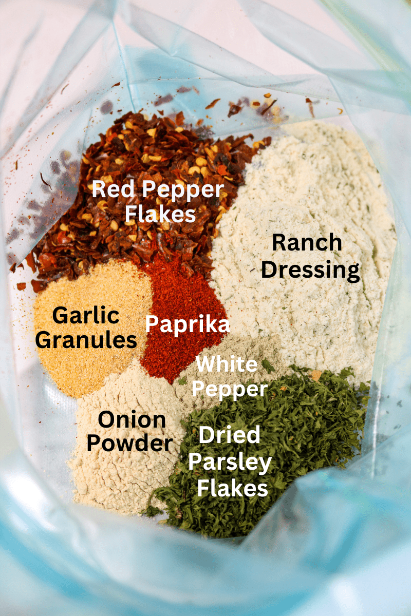 A glass bowl with red pepper flakes, ranch dressing, paprika, garlic granules, onion powder, white pepper, and parsley flakes.