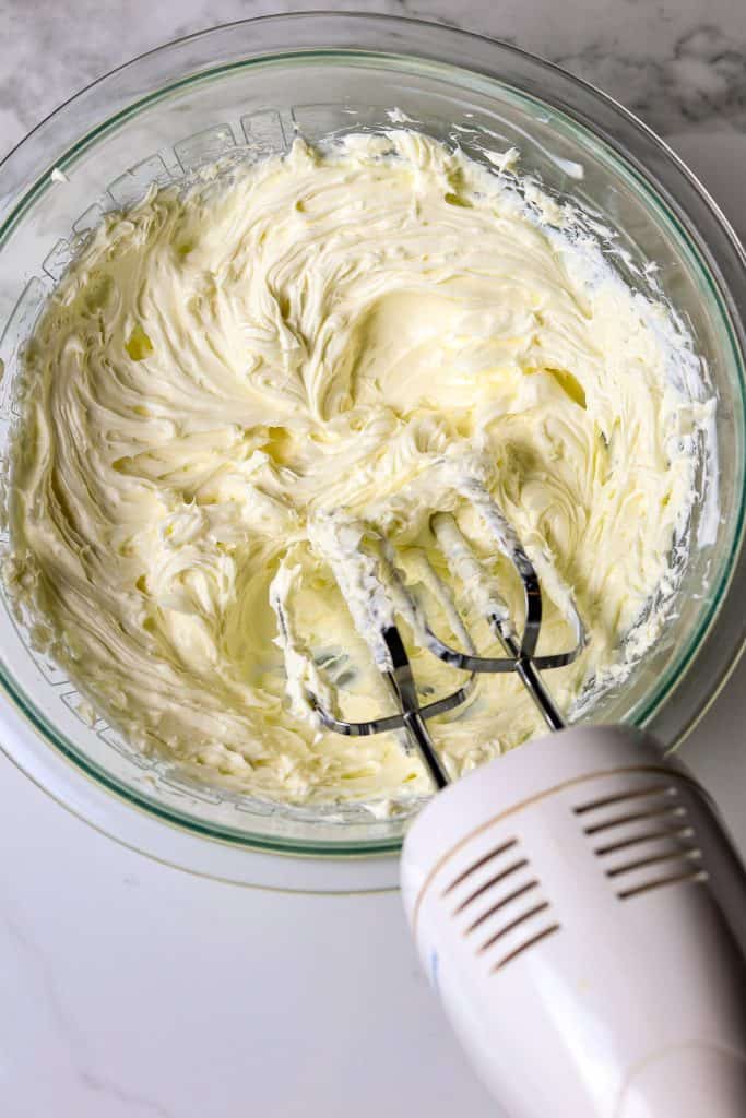 A glass bowl of creamed cream cheese with mixer beaters in the cream cheese.