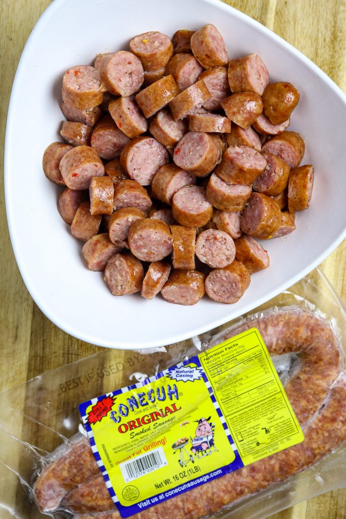 Slices of smoked sausage in a white bowl on a wooden cutting board.