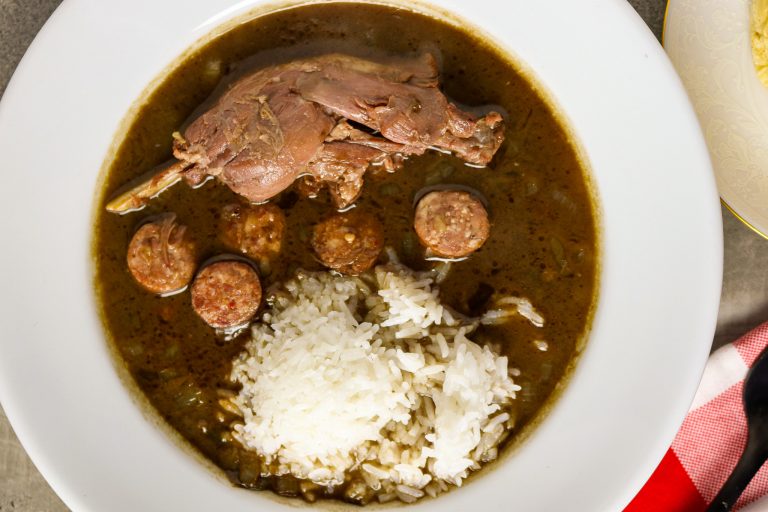 A white bowl of Goose Gumbo with a scoop of rice in it and a pice of meat that looks like a running Razorback.