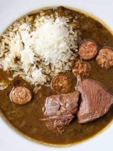 A white bowl of Goose Gumbo with a scoop of rice in it and a pice of meat.