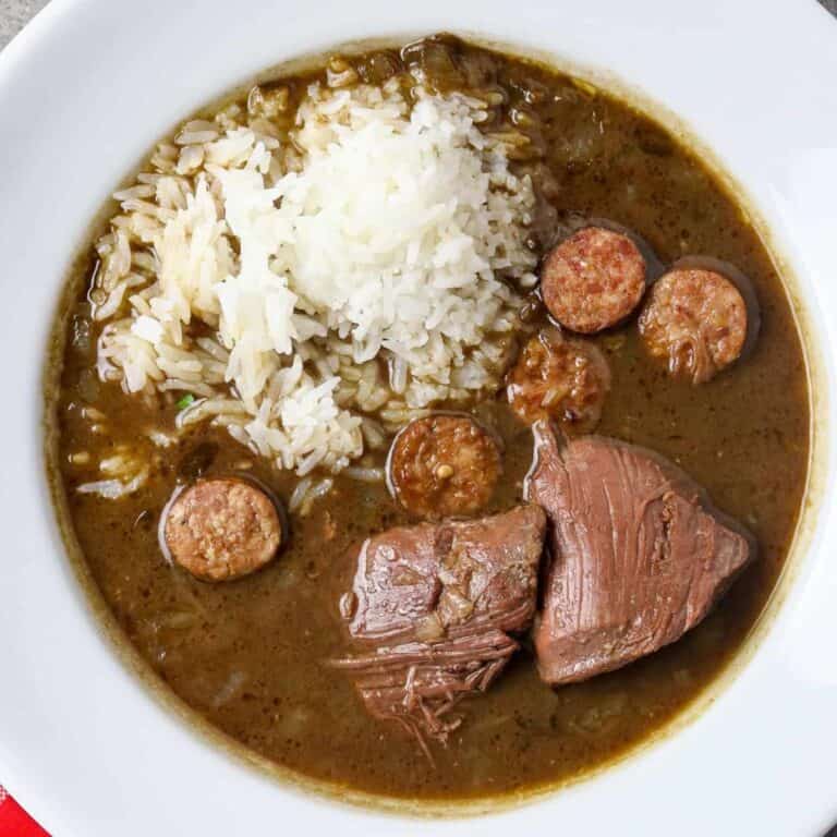 A white bowl of Goose Gumbo with a scoop of rice in it and a pice of meat.