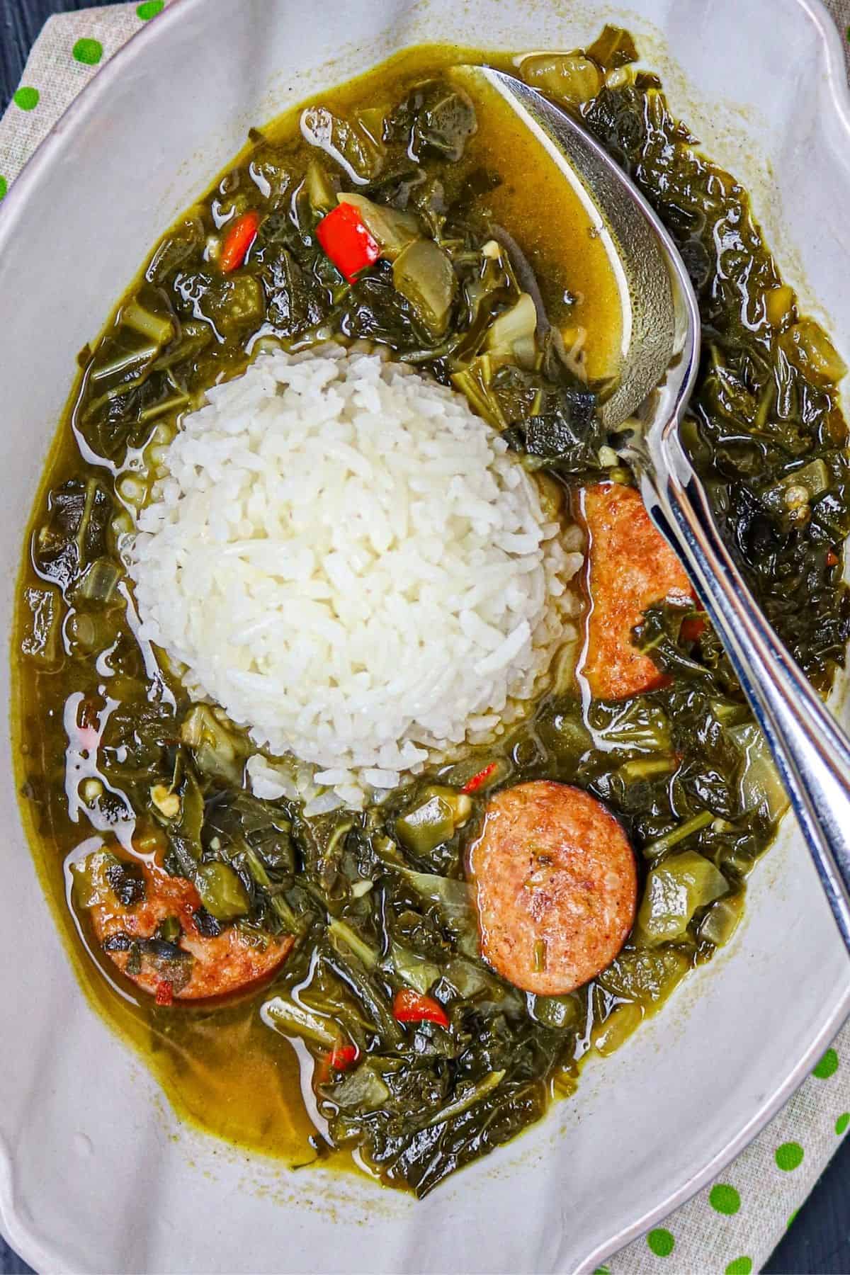 A white bowl of greens in a gumbo sauce with sausage and a mound of white rice in the center.