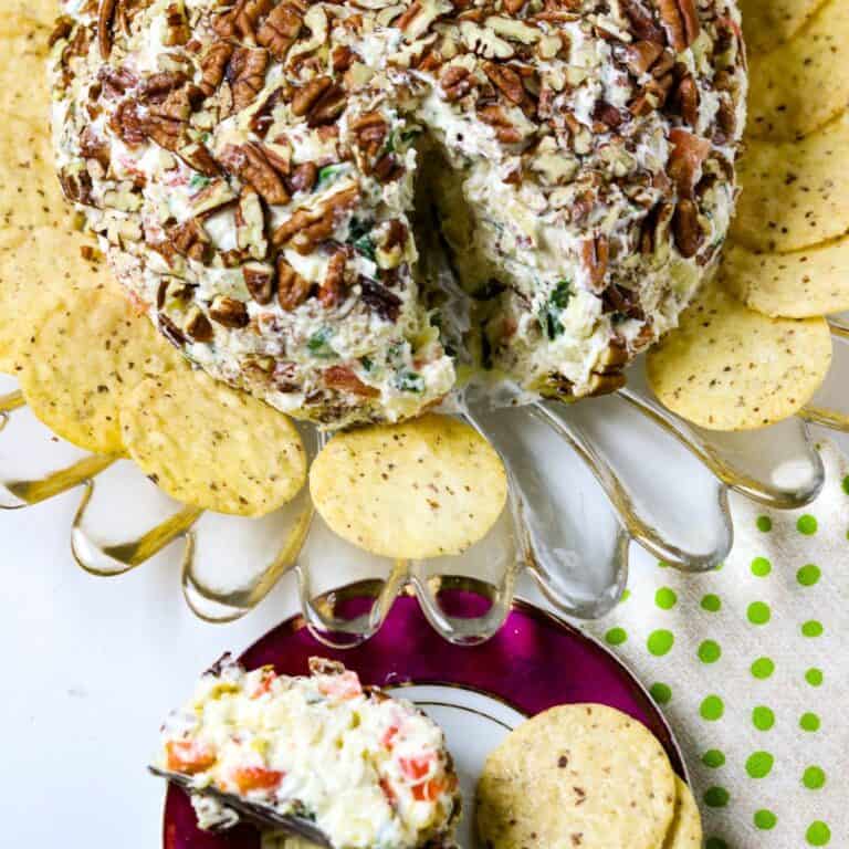 A Pineapple Cheese Ball on a glass plate with a spreader and a dish of cheeseball with crackers beside it.