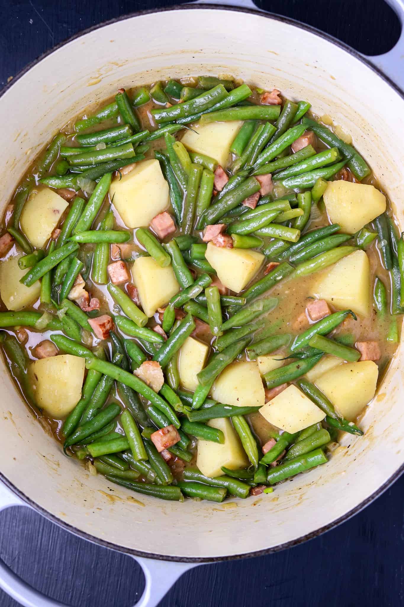 A pot is full of smothered green beans with potatoes and ham.