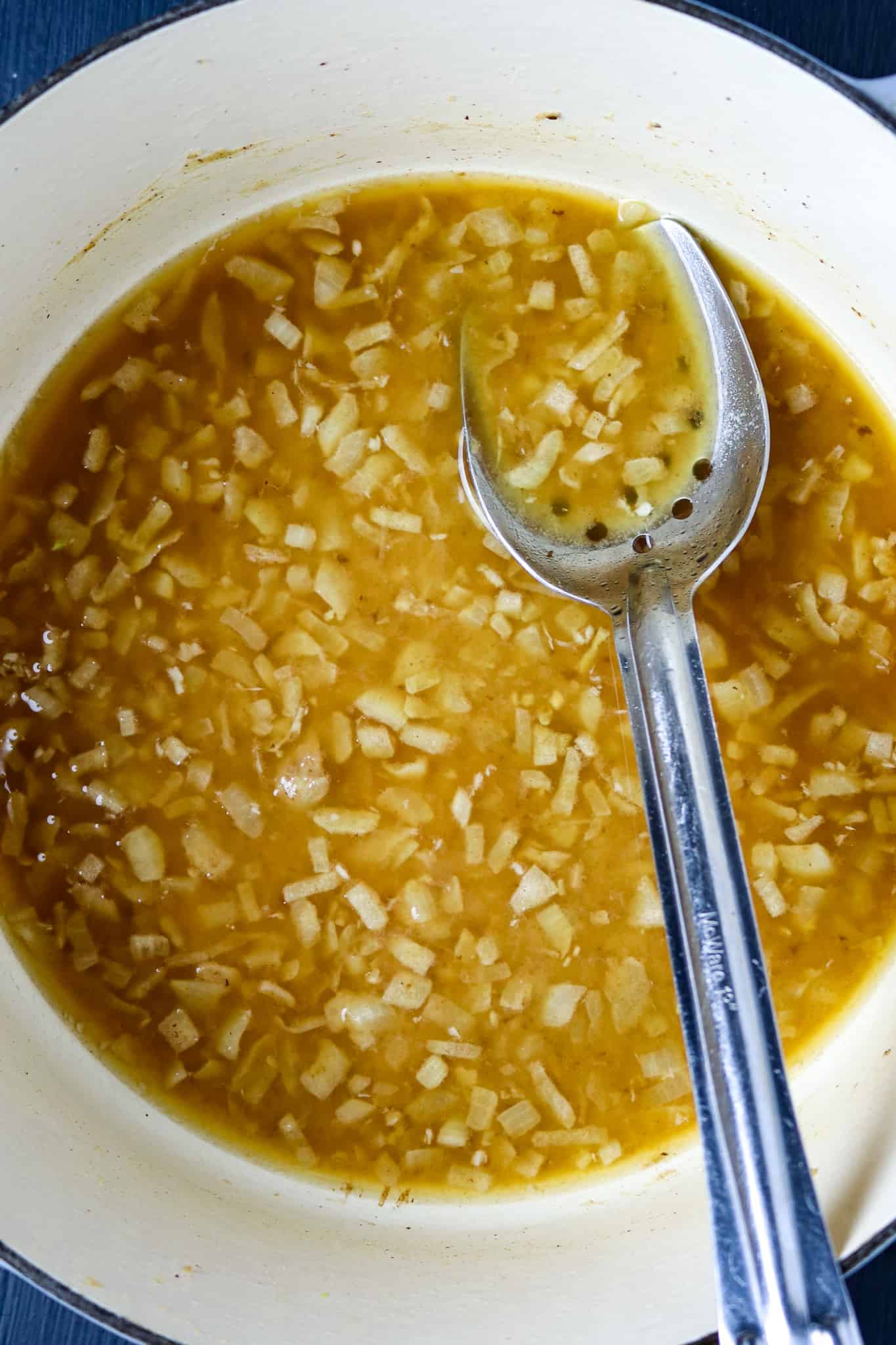 Spoon stirring a pot of broth with cooked onions.