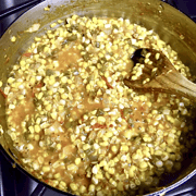 A pan of Corn Maque Choux and a wooden spoon in it.