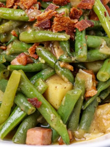 Green beans cooked with potatoes garnished with bacon bits.