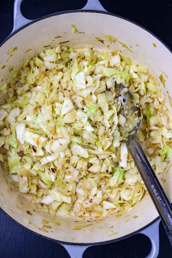 Smothered cabbage with onions in a pot with a long-handled spoon.