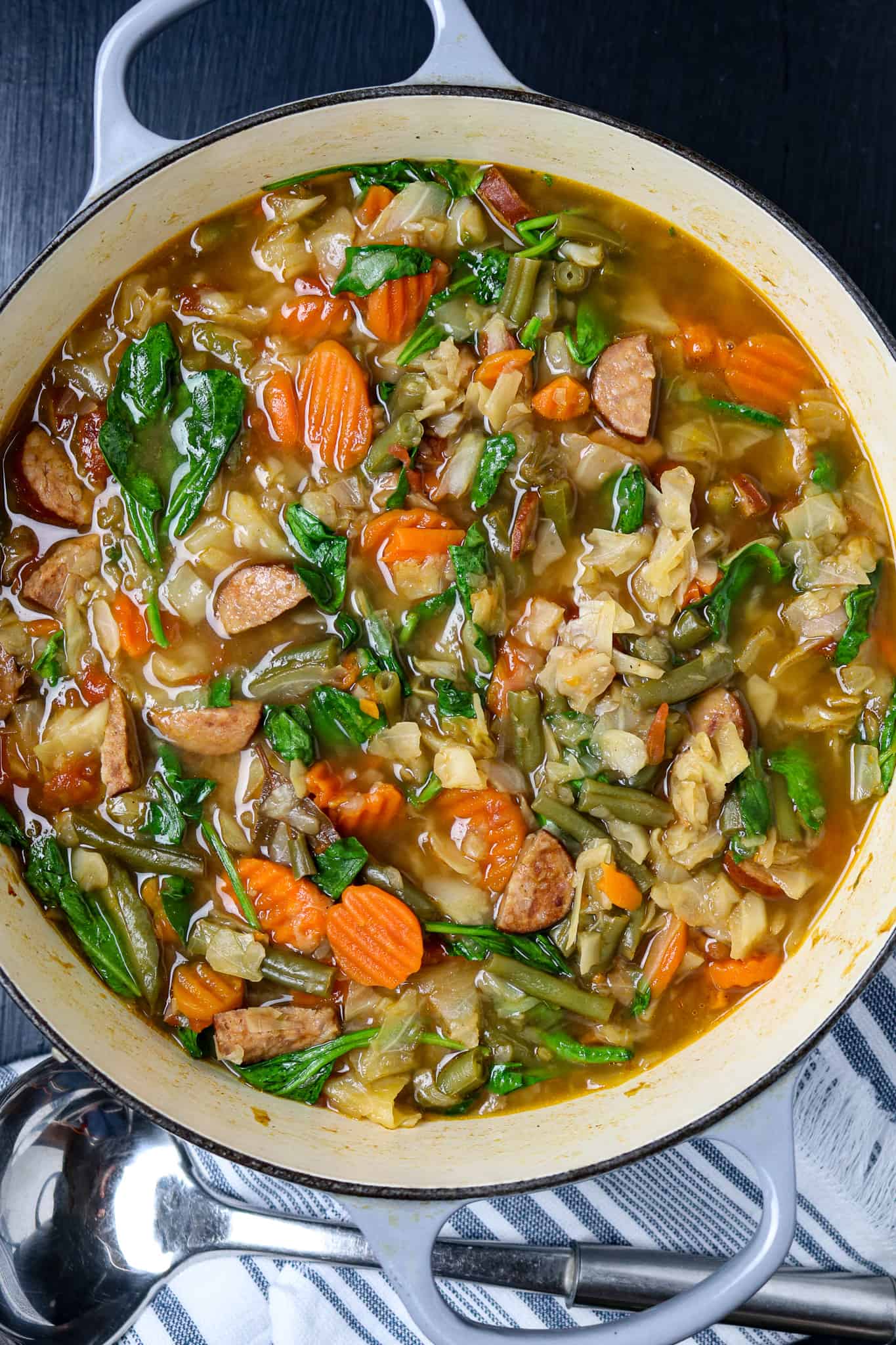 A pot of vegetable soup with cabbage carrots, spinach, green beans, and sausage.