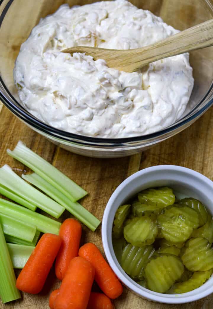 A glass bowl of creamy dip with pickles, celery, and carrots beside it.