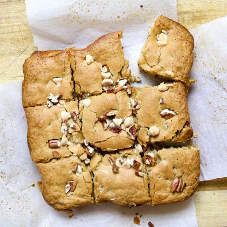 A square of blonde brownies cut into 9 pieces on parchment paper and a wooden cutting board.