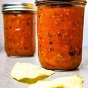 Two mason jars of roasted salsa and a few tortilla chops beside them.