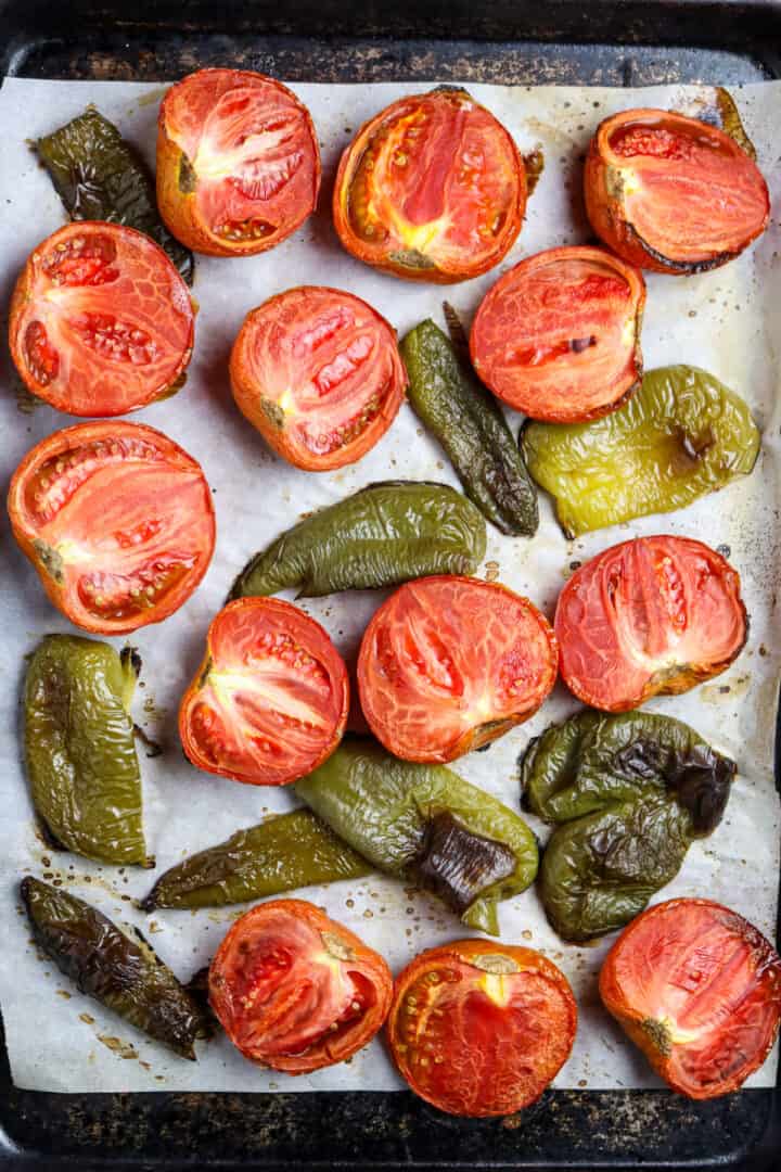 Single layer of roasted tomatoes and green peppers on a sheet pan for roasted salsa.