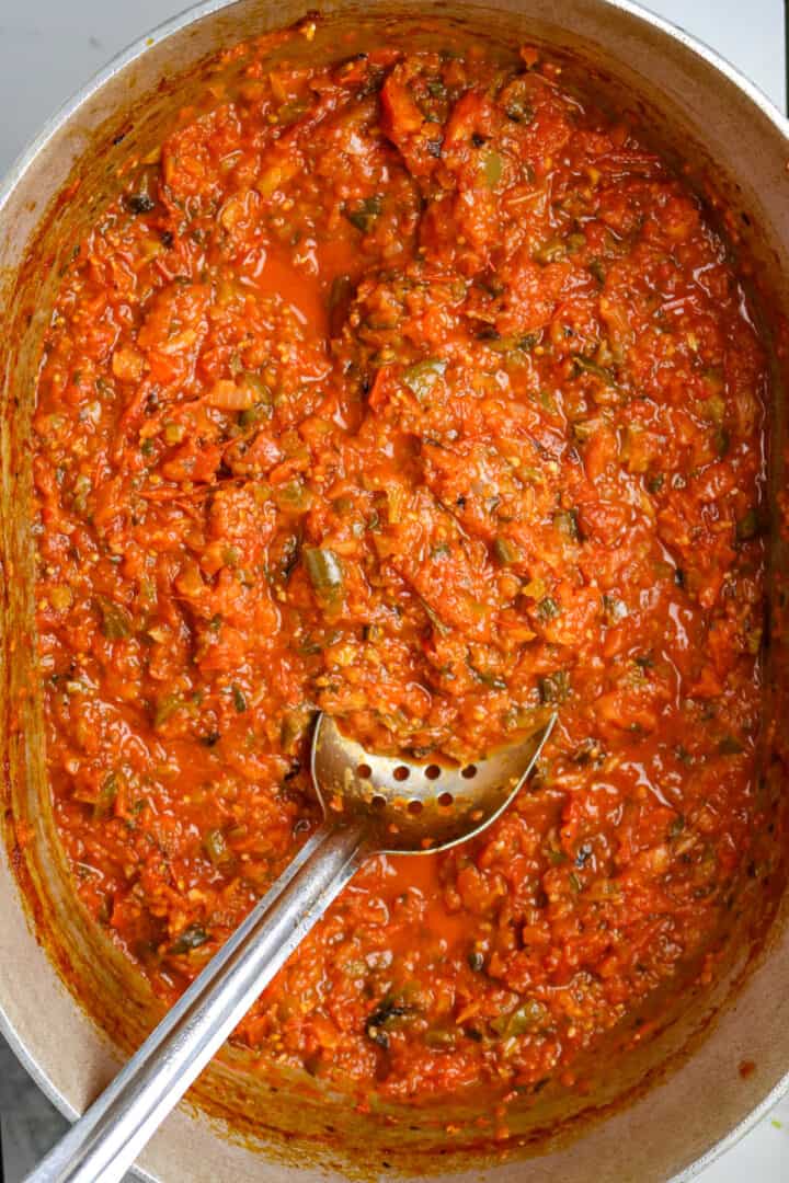 A large pot of roasted salsa with a long handled silver spoon before it is cooked.