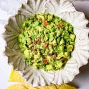 Guacamole in a white bowl with chips scattered on the outside of it.