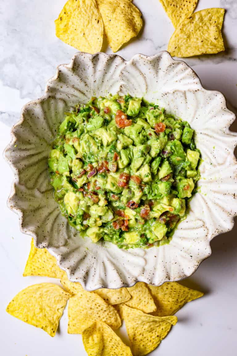 Guacamole in a white bowl with chips scattered on the outside of it.