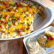 An oblong light gray pottery dish with baked dip in it topped with cheese bacon bits, and sliced green onions.