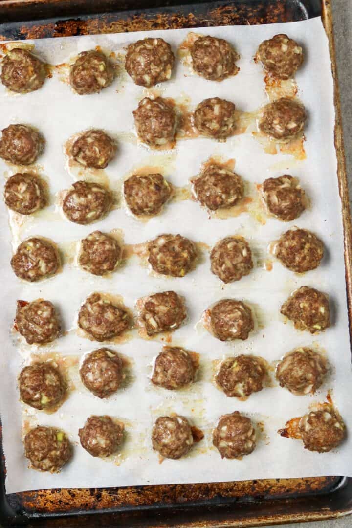 Small cooked meatballs lined up on a paper-lined cookie sheet.