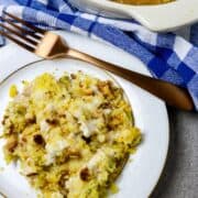 A pan of Easy Farmhouse Chicken Casserole next to a plate of it and a fork resting on the plate.