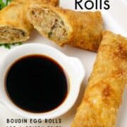 A long white plate with cup of soy sauce and cut egg rolls around it.