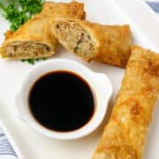 A long white plate with cup of soy sauce and cut egg rolls around it.