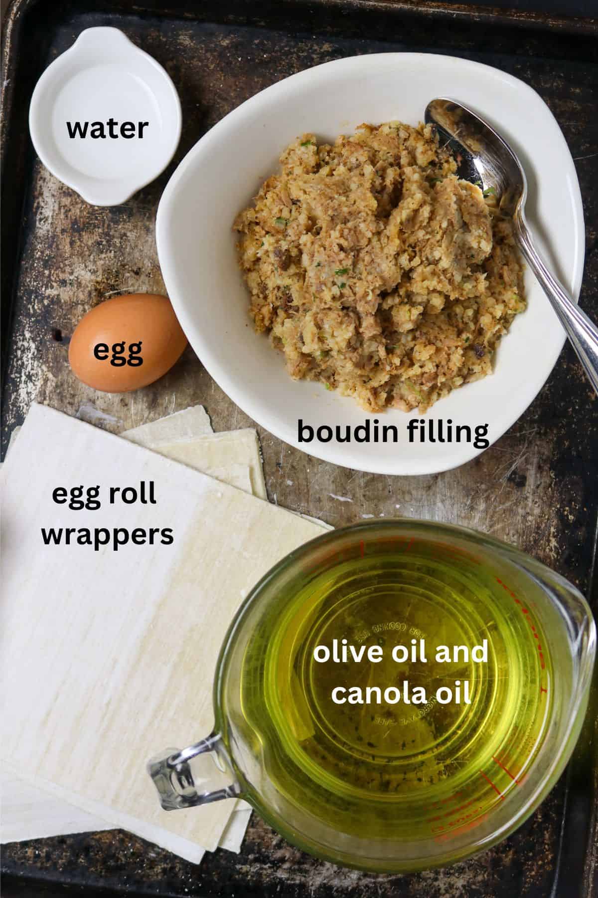 A white bowl of boudin stuffing next to an egg roll wrap, and egg, and a measuring cup of oil.