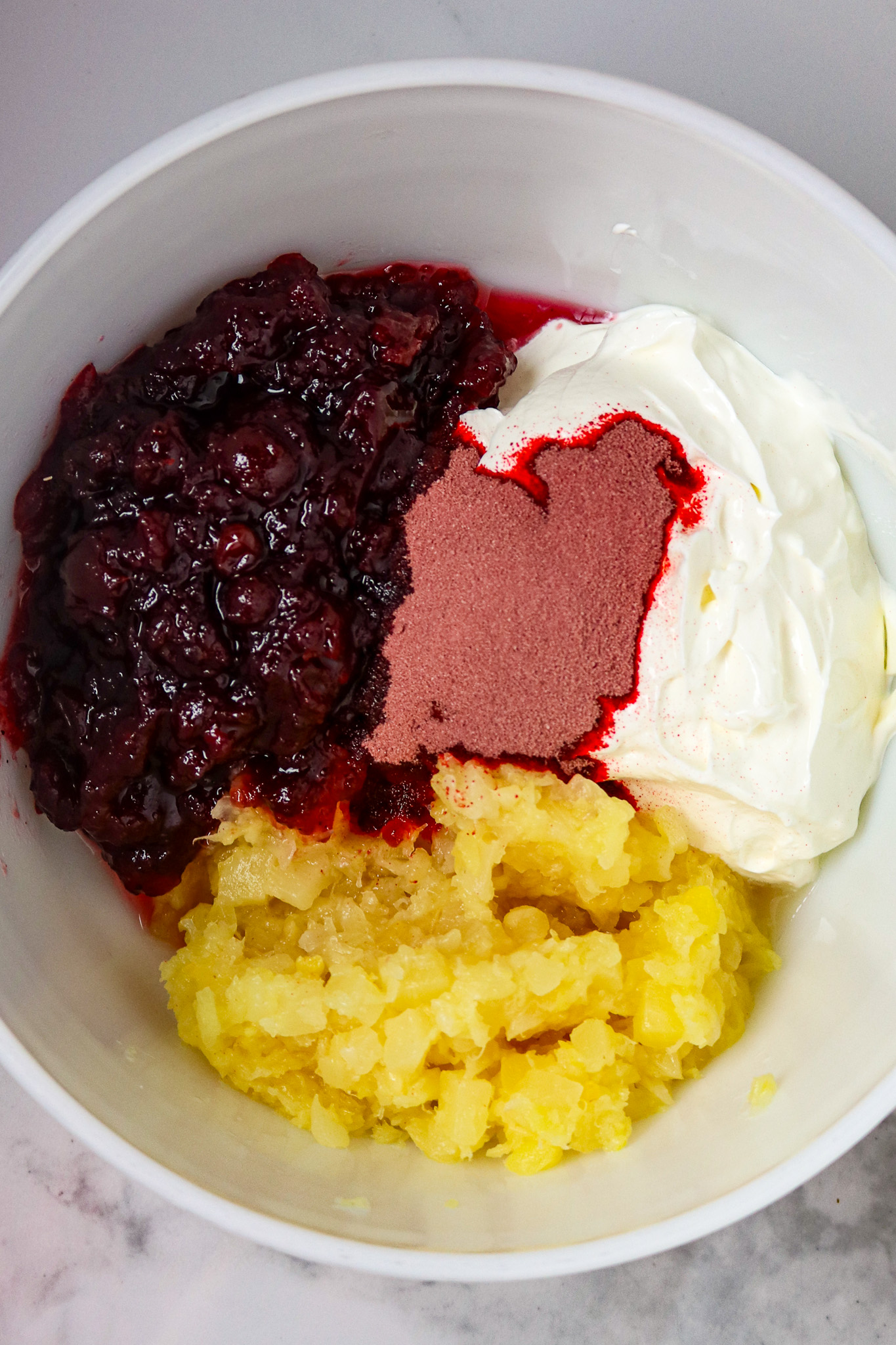 A white bowl of sour cream, cranberry sauce, jello, and pineapple.