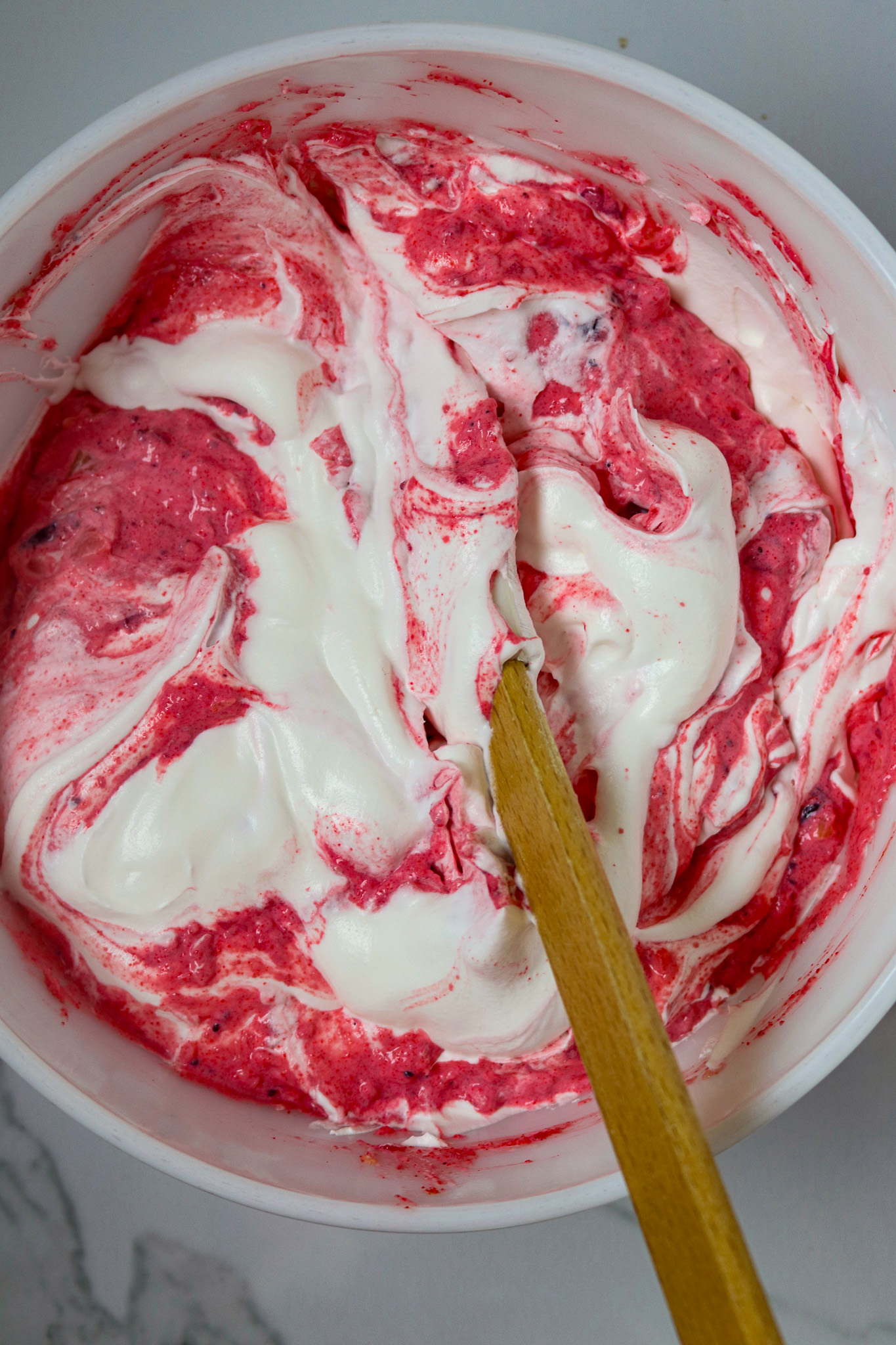 A bowl of cranberry salad mixture with a spoon folding in whipped topping.