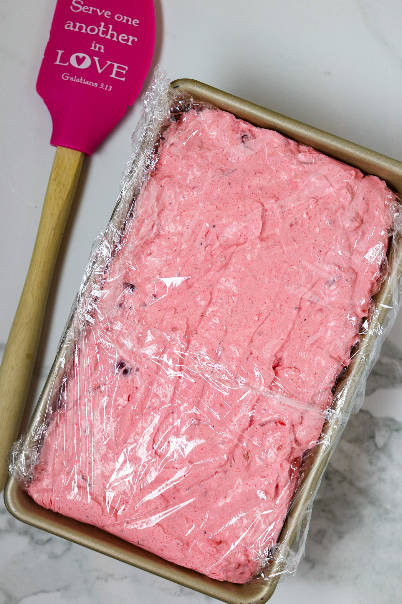 A bread loaf pan filled with pink whipped topping dessert,