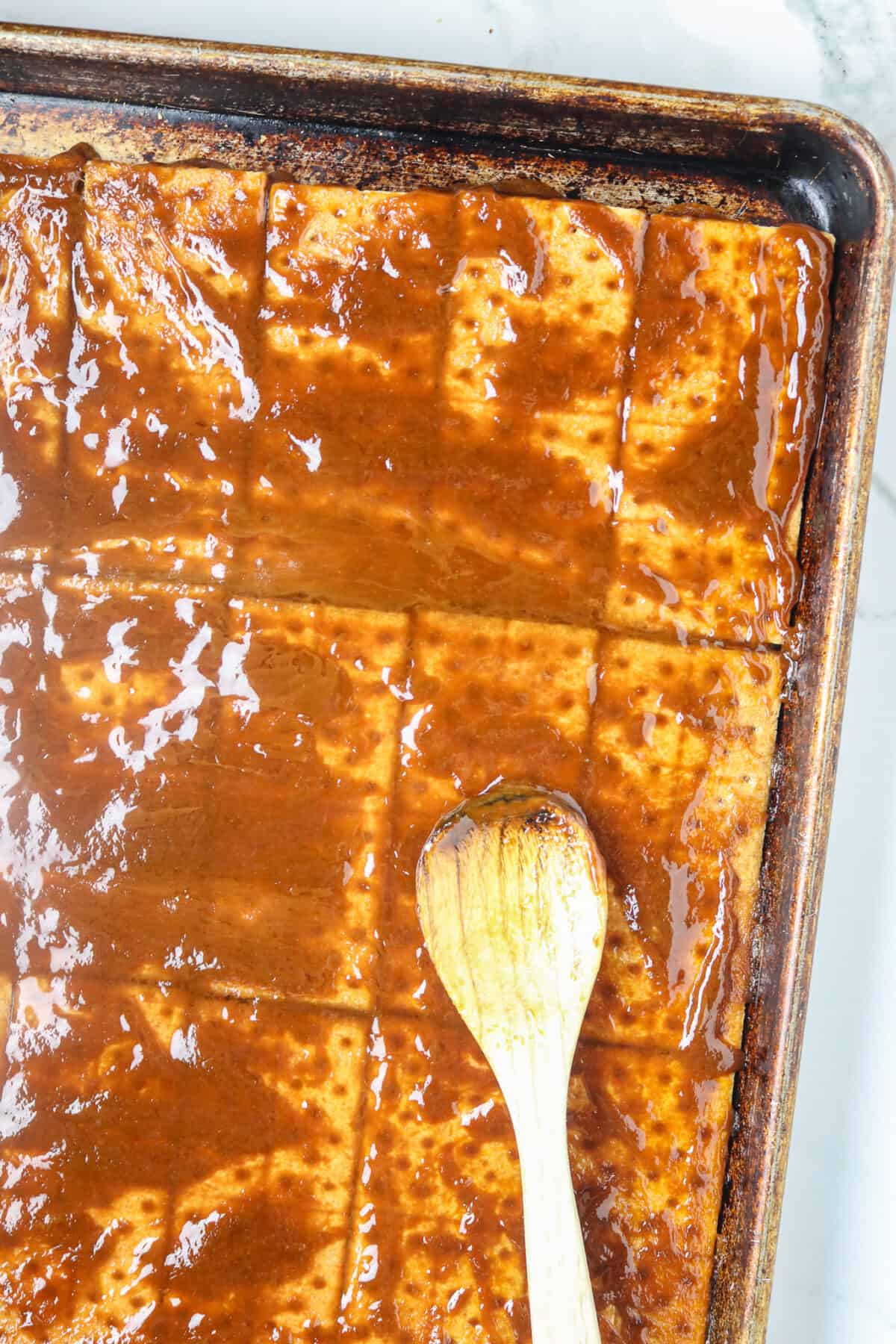 A wooden spoon spreading toffee on top of graham crackers.