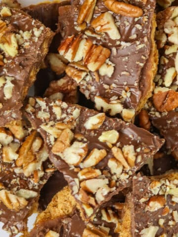 A mound of nut topped Easy Graham Cracker Oven Toffee in different shapes and sizes on a white plate.