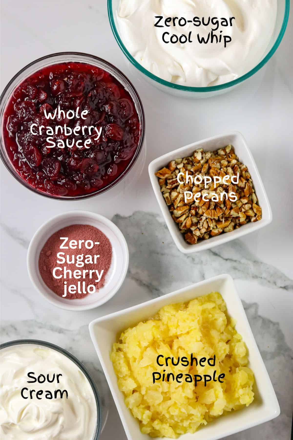 Ingredients of cranberry sauce, sour cream, pineapple, jello, whipped topping, and pecans in individual containers on a countertop.