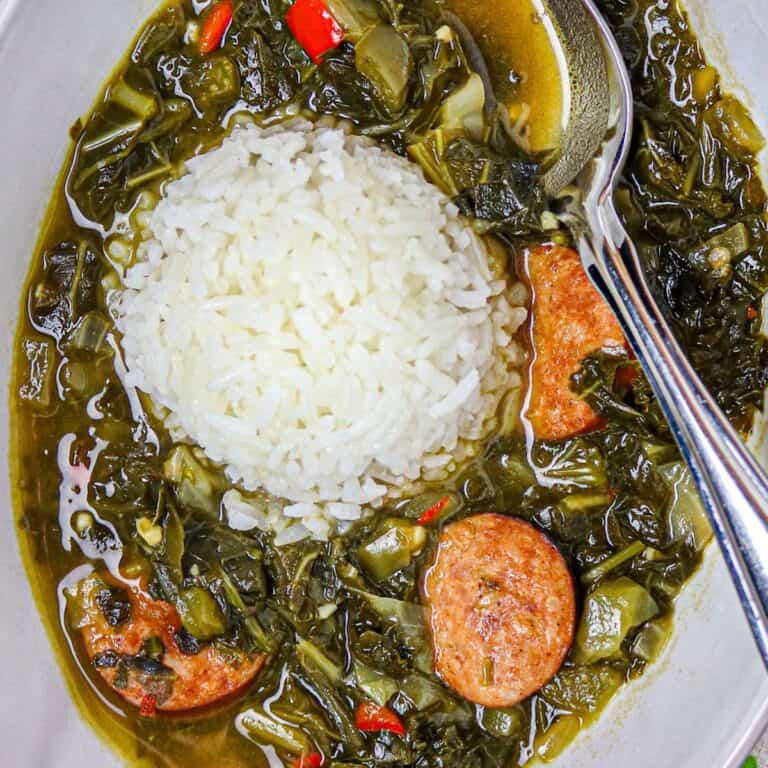 A bowl of green gumbo with a scoop of white rice and a silver spoon.