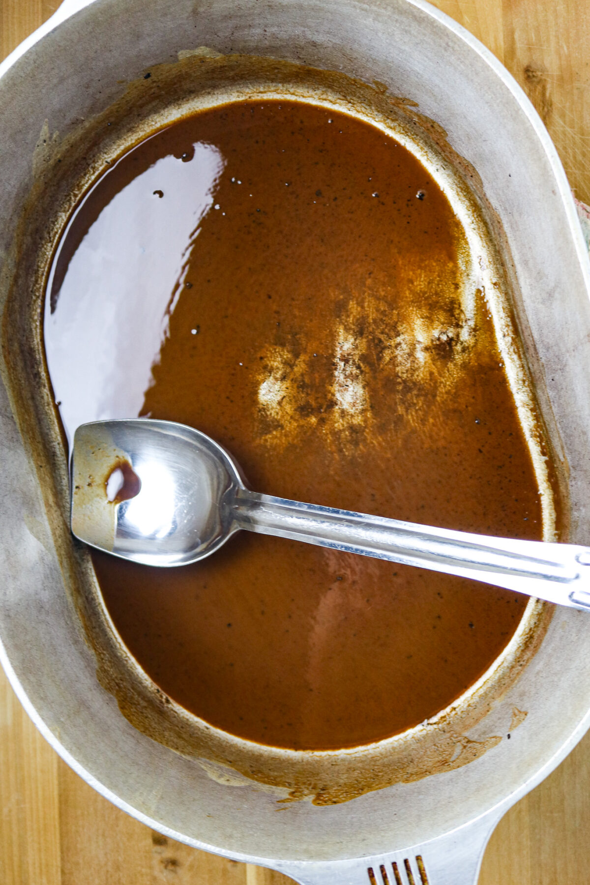 A large pot of dark roux with a silver spoon in it.