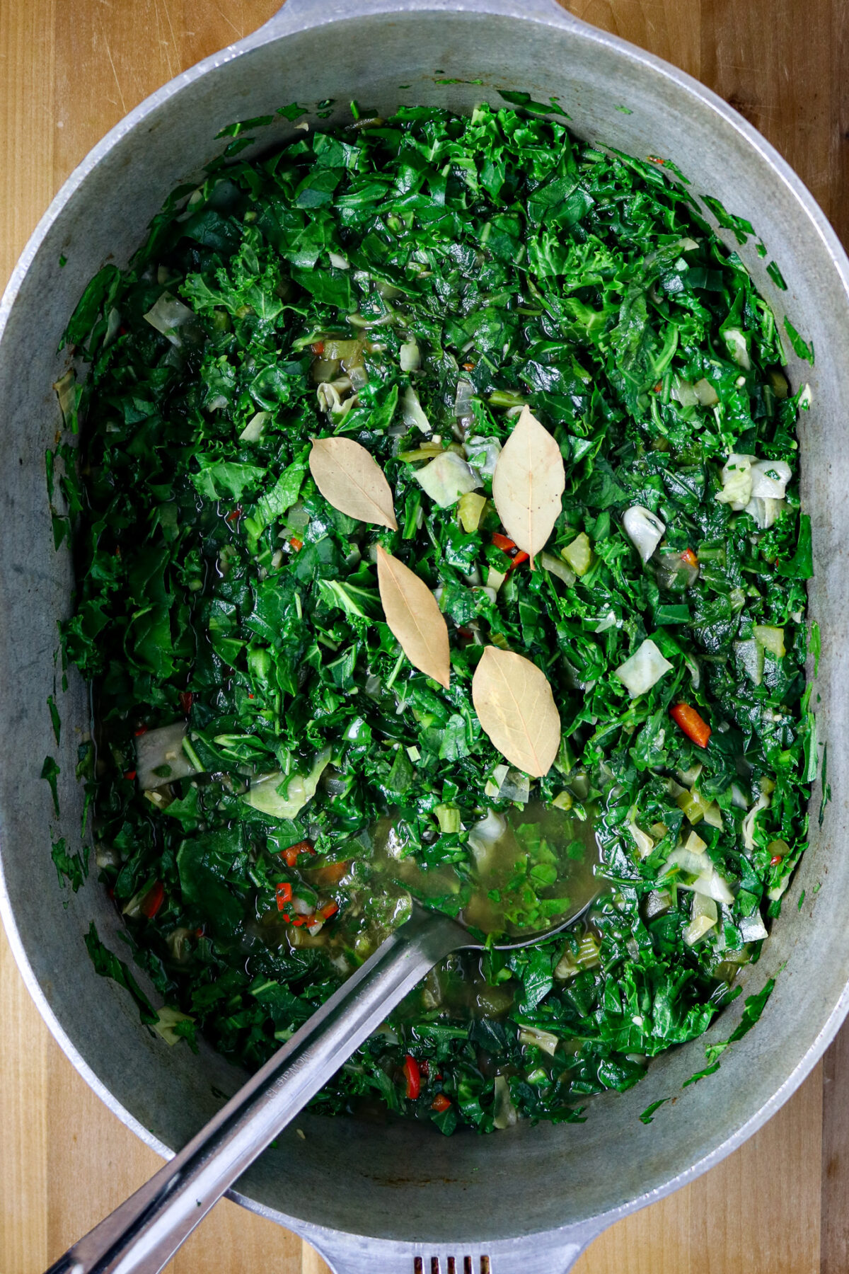 A large pot of greens for gumbo zherbes' with four bayleaves laying on top.