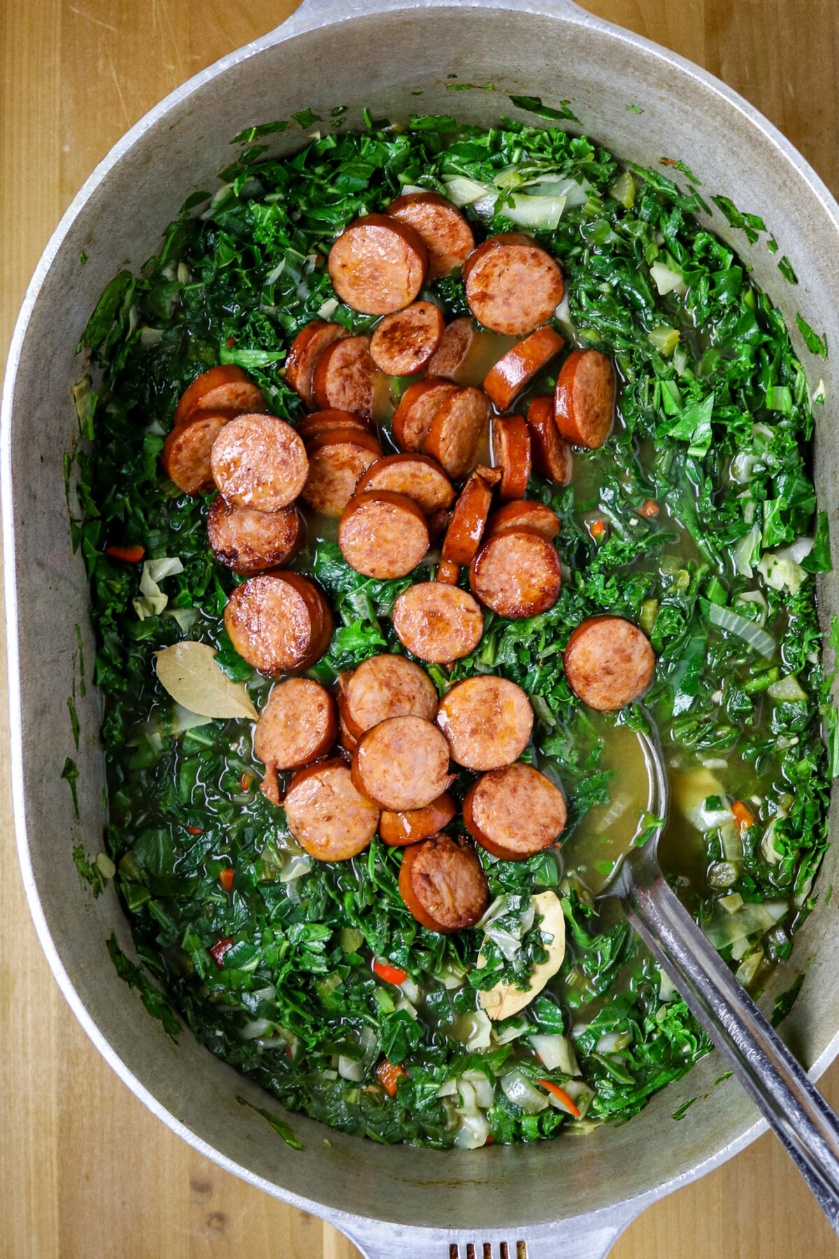 A large pot of green gumbo with slices of sausage laying on top of it.