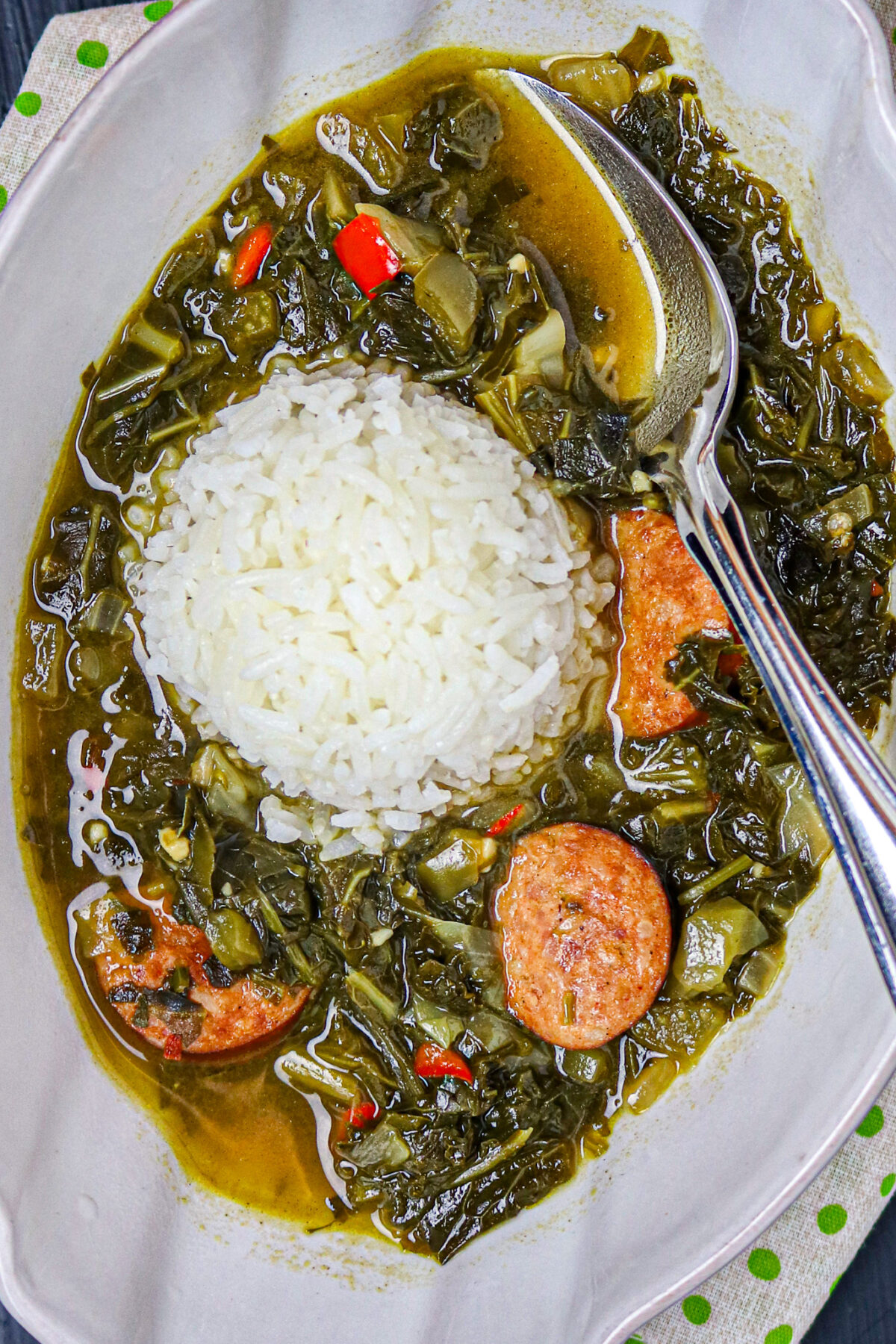 A bowl of gumbo zHerbes' with a scoop of white rice and a silver spoon in it.