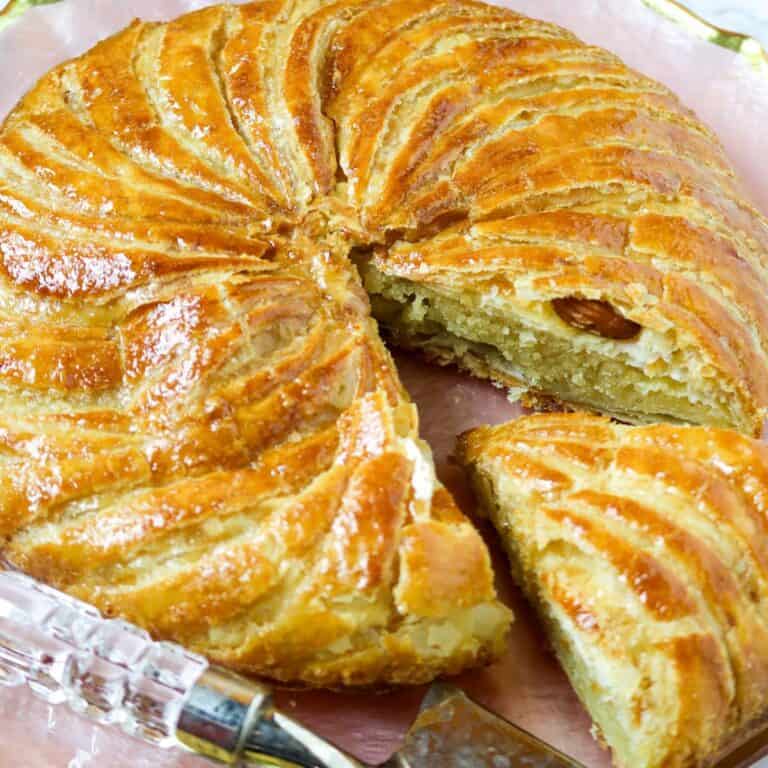 A round pastry cake with a slice cut out exposing a whole almond.
