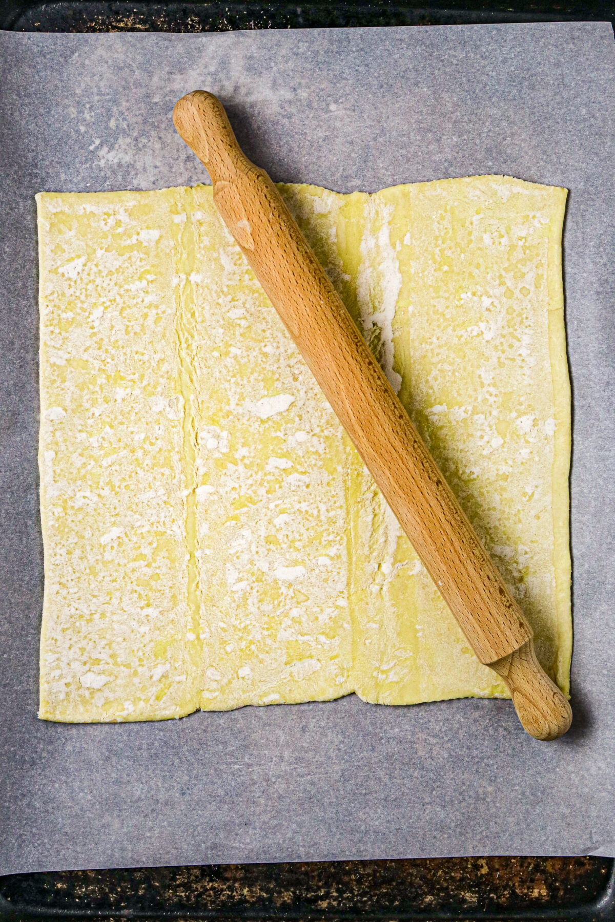 A wooden rolling pin in the middle of a square of puff pastry.
