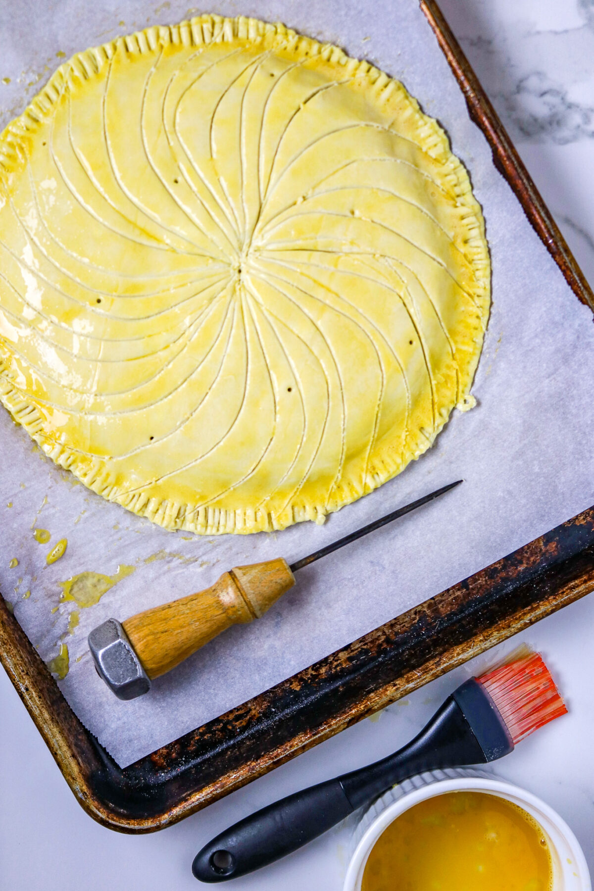 An unbaked round puff pastry for a Galette Des Rois with an ice pick next to it.